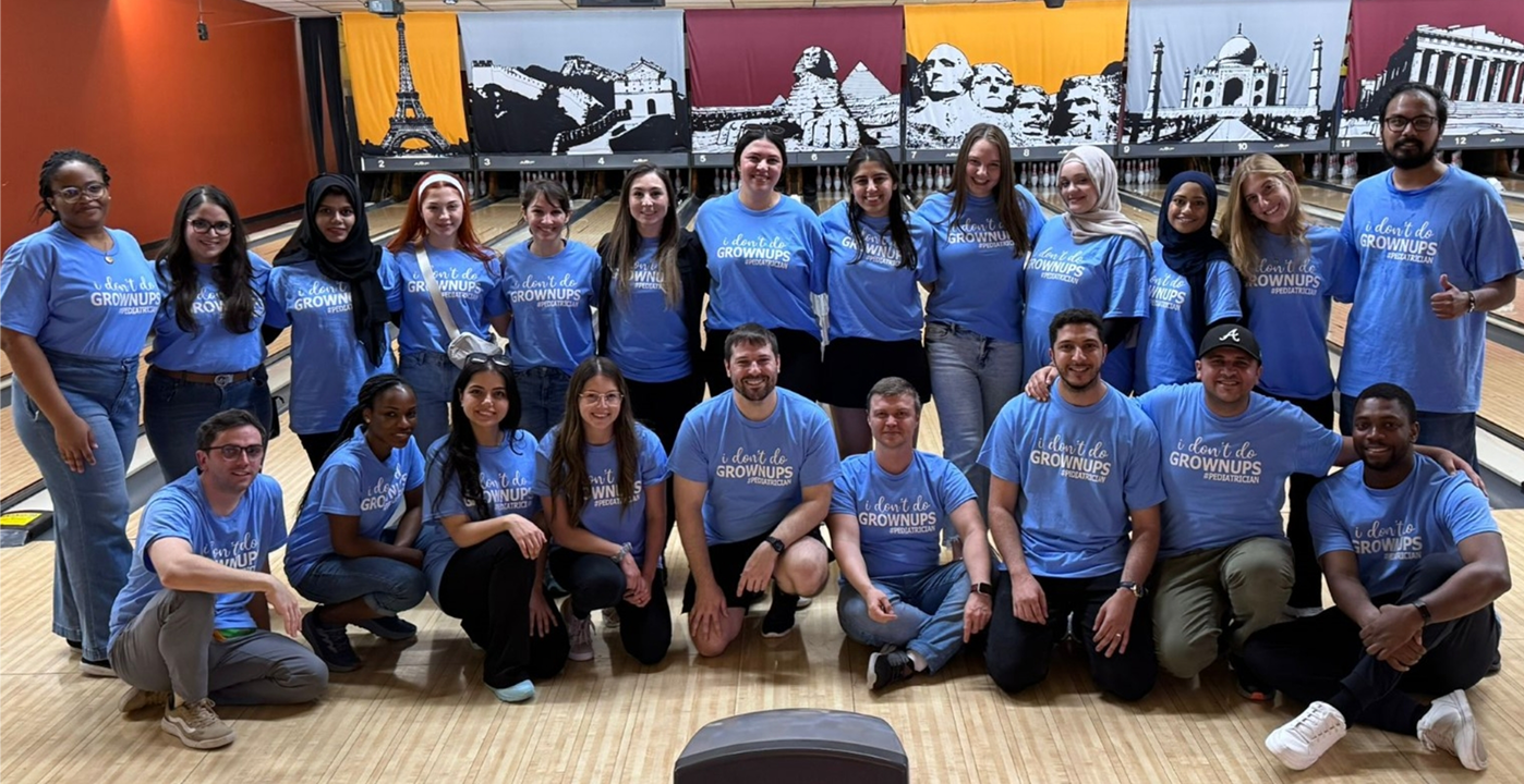 Group of medical residents in matching blue T‑shirts posing on a bowling lane during a team wellness event.