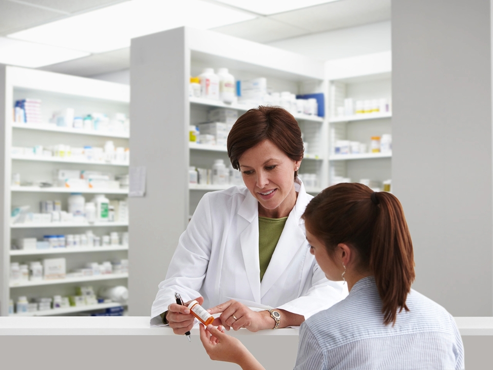 Pharmacist in a white coat speaks with a woman while looking at her prescription