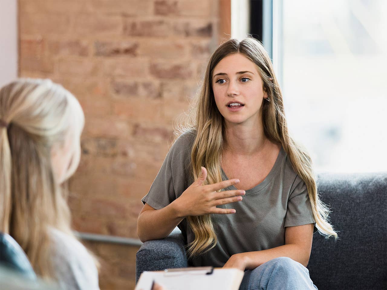 Young woman in a grey shirt speaks to a counselor during a therapy session