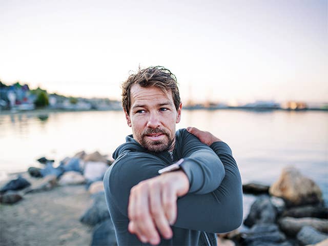Man in wetsuit stands in front of lake stretching