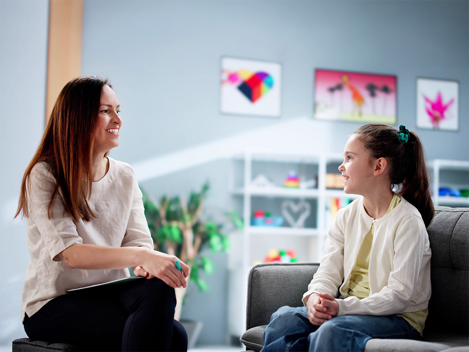 Adult seated across from a child during a conversation in a structured indoor setting.