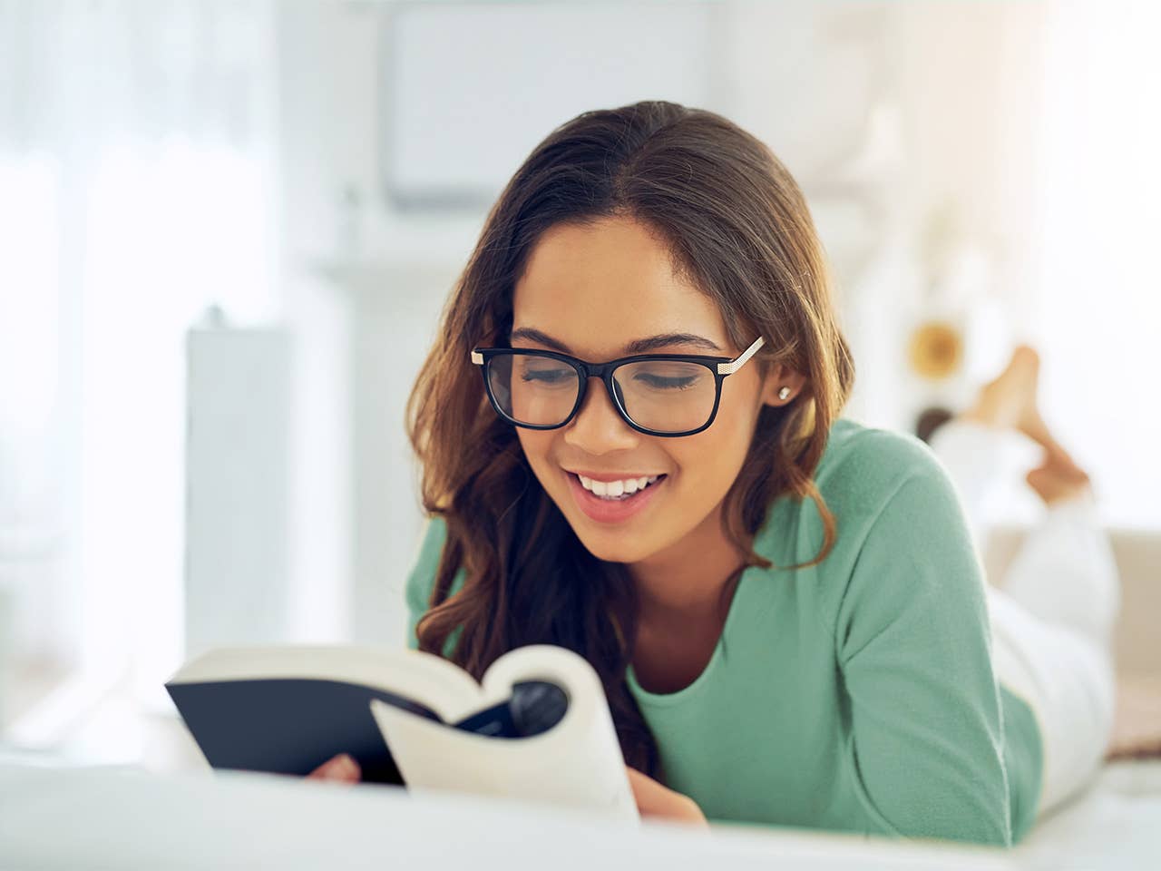 Smiling young woman with brown hair and glasses reads a book