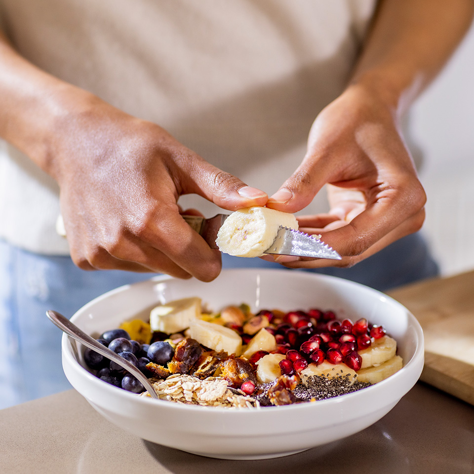 Man's hands cutting banana into a bowl of fruit