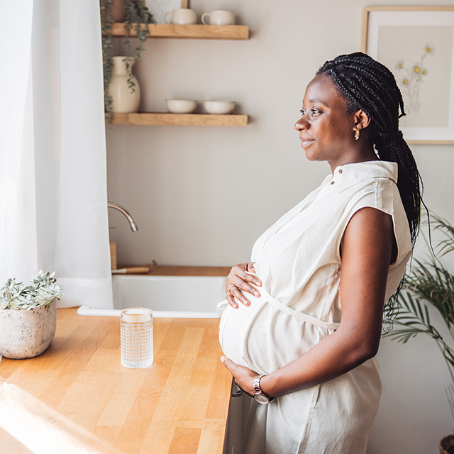 Smiling pregnant Black woman stands near the kitchen counter in a sunlit room