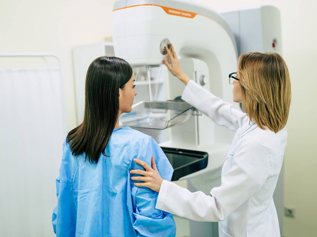 Corewell Health breast imaging specialist assists a patient as she stands in front of a mammography system