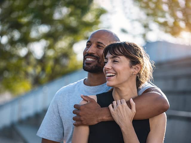 A man and woman smile warmly while embracing each other in a joyful moment.