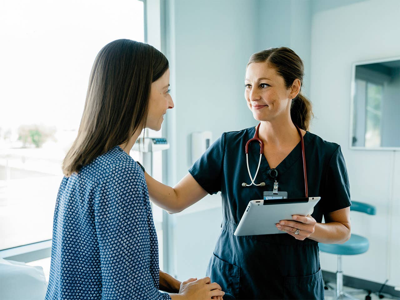Woman with shoulder length brown hair speaks with a nurse in a primary care office
