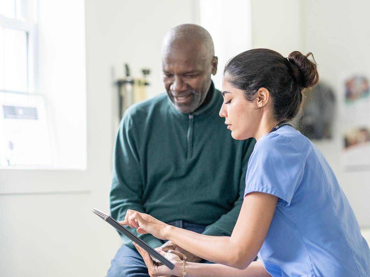 Middle aged Black man wearing a dark green sweater sits next to a Corewell Health employer services team member in an exam room