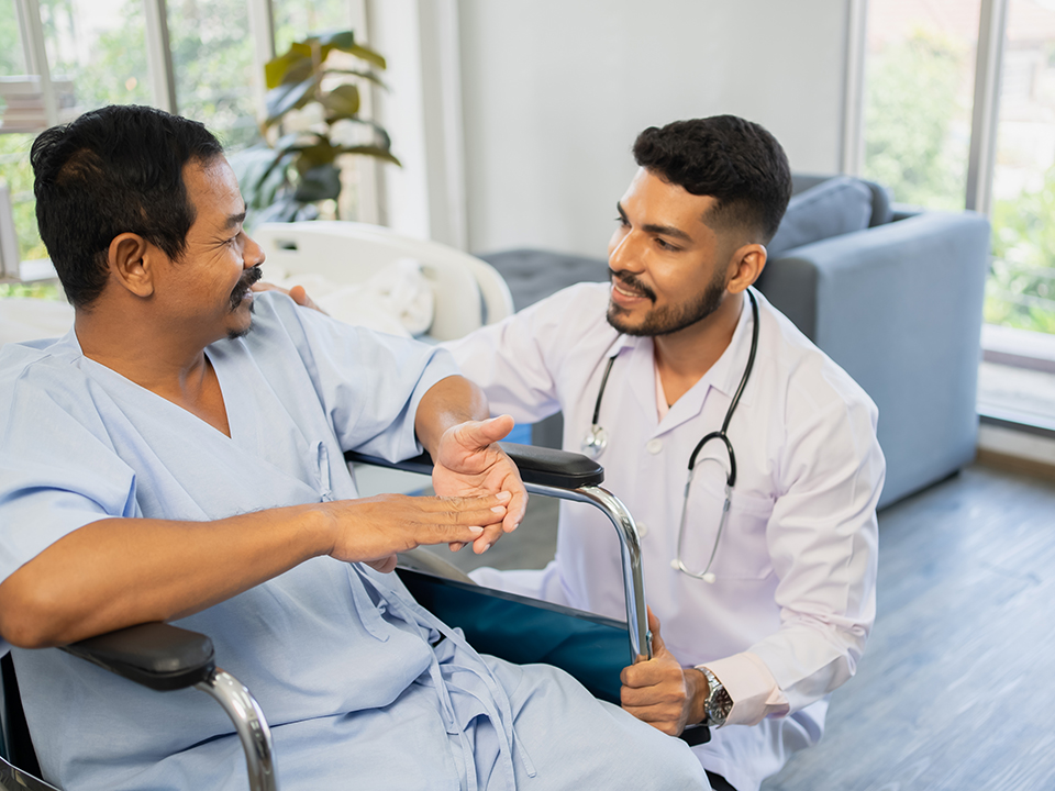 A male doctor converses with a patient seated in a wheelchair during a medical consultation.