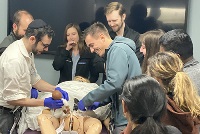 A diverse group of individuals engaged in discussion around a mannequin during a simulation activity.