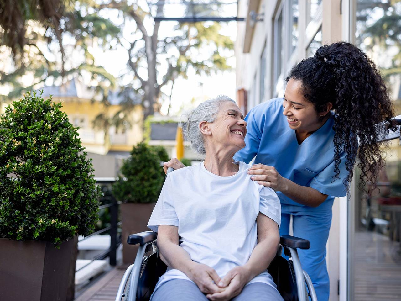 A nurse assists an elderly woman in a wheelchair, providing support and care.