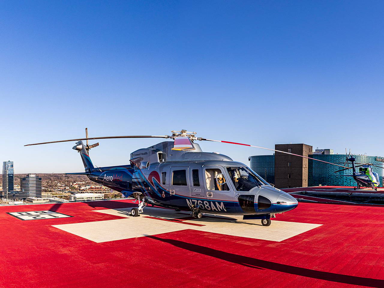 Corewell Health Aero Med helicopter, with silver and blue paint on its body, sitting on a helipad on top of a building
