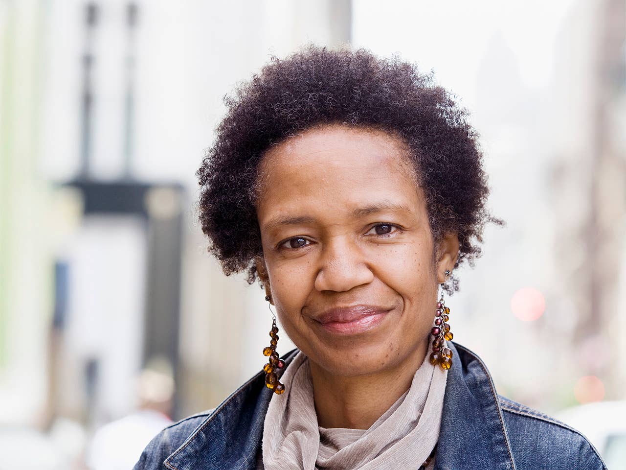 Black woman with short curly hair stands outdoors wearing a denim jacket