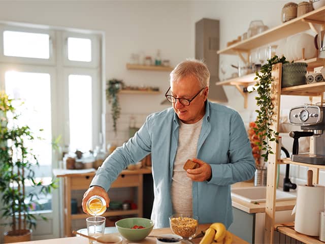 Older adult preparing a nutritious breakfast with fruit, cereal and juice in a home kitchen to support dietary needs.