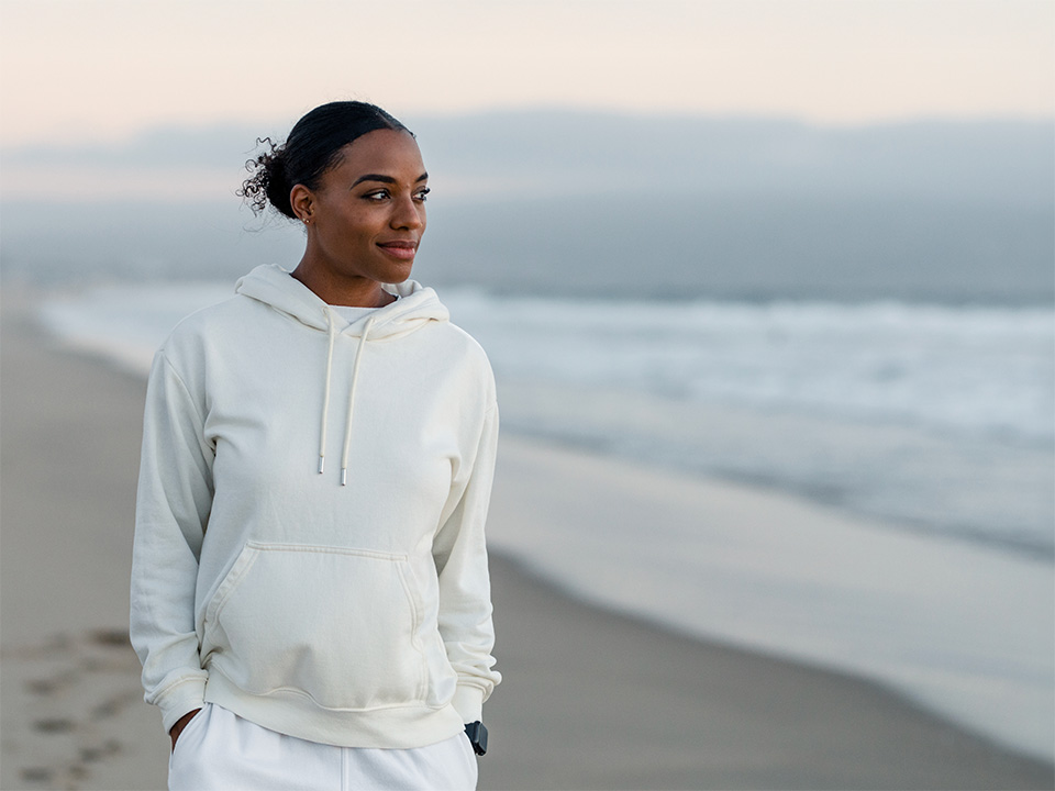 A woman in a white hoodie stands on the beach.