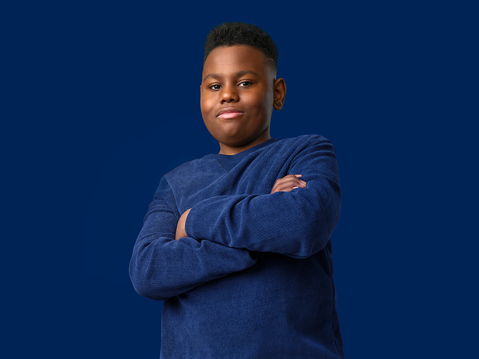 Teenage Black boy wearing a navy blue sweater stands proudly with his arms crossed over his chest