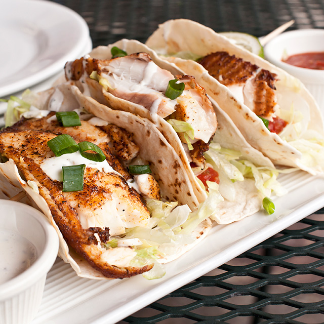Plate of fish tacos topped with lettuce and green onions, served with sauce as a fresh, flavorful meal.