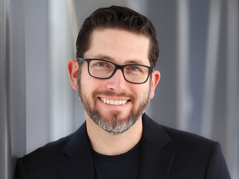 Alejandro Quiroga, MD, middle aged man with dark brown hair, glasses and beard, wearing a black sport coat and black shirt