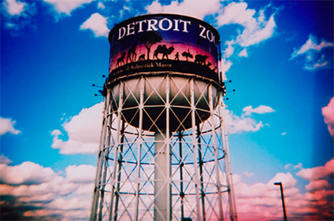 A water tower displaying a sign that reads "Detroit Zoo," situated in a vibrant area with various recreational activities.
