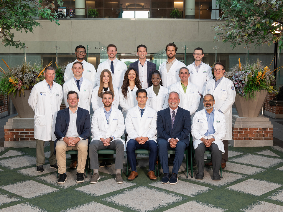 Group portrait of 16 medical professionals and residents in white coats posed in a hospital atrium.