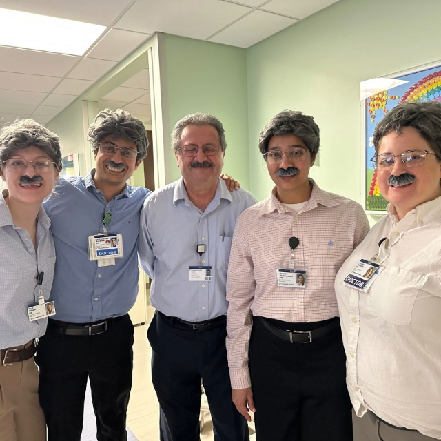 Group of fellows posing in wigs and glasses along with a doctor they were imitating
