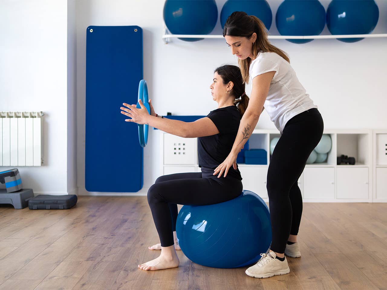 Occupational therapist helps a woman balance as she sits on an exercise ball while holding a weighted disc