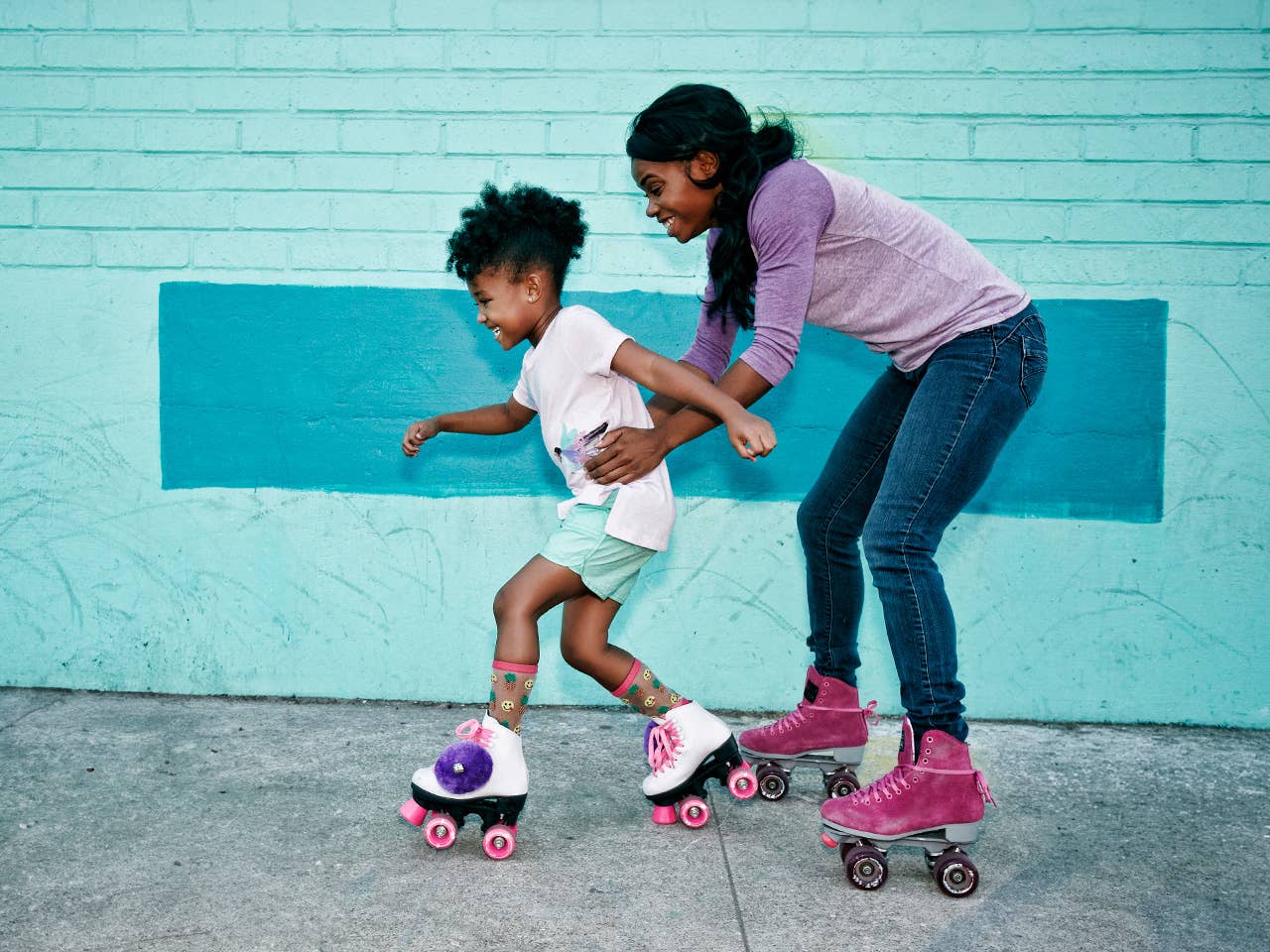 Two African American girls roller skating together in front of a brick wall