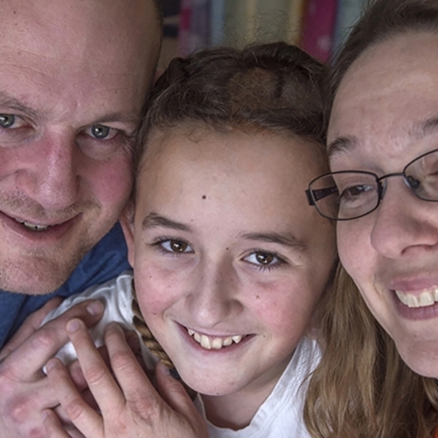 Smiling preteen girl hugs her smiling mother and father