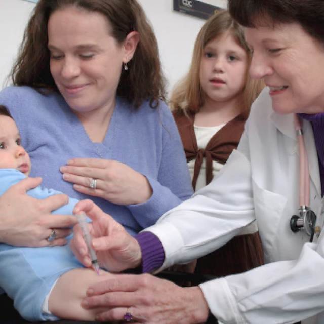 Smiling mom holds a baby while doctor listens to its heartbeat