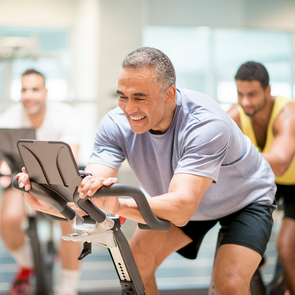 Smiling man with short grey hair on a stationary bike as part of a spin class