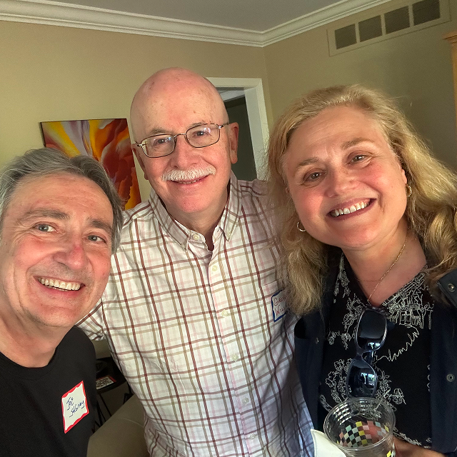 Three attendees pose together indoors at a social gathering, with one person holding a drink.