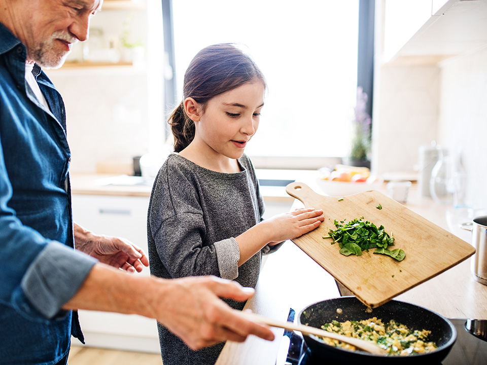 Older man cooks in kitchen with his granddaughter