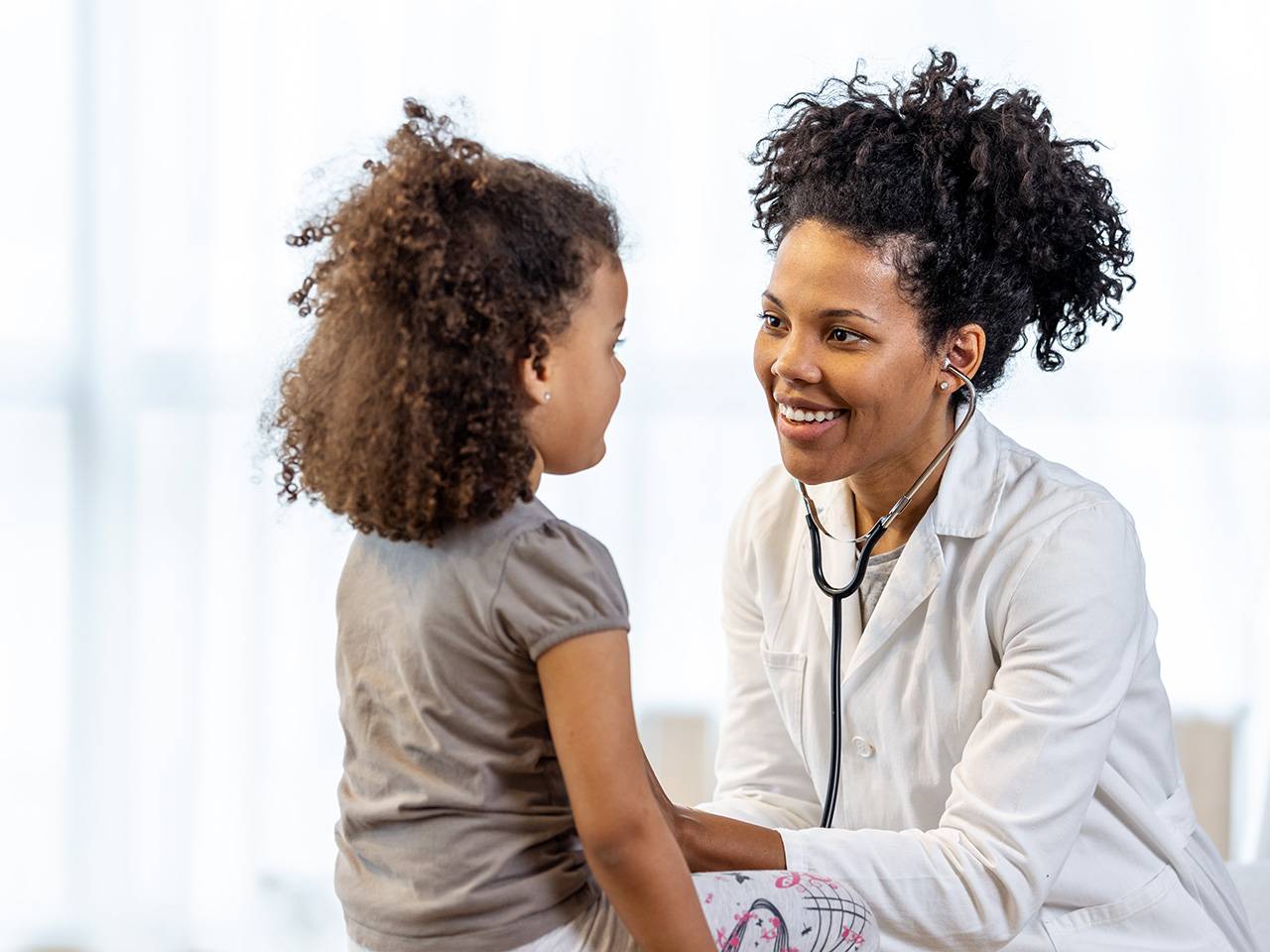 Healthcare provider using a stethoscope to examine a young child during a pediatric visit.
