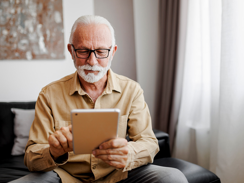 older male sitting on his couch scheduling a doctors appointment through his tablet