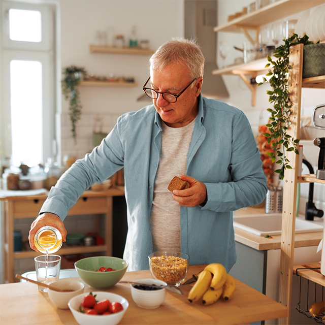 Older adult preparing a nutritious breakfast with fruit, cereal and juice in a home kitchen to support dietary needs.