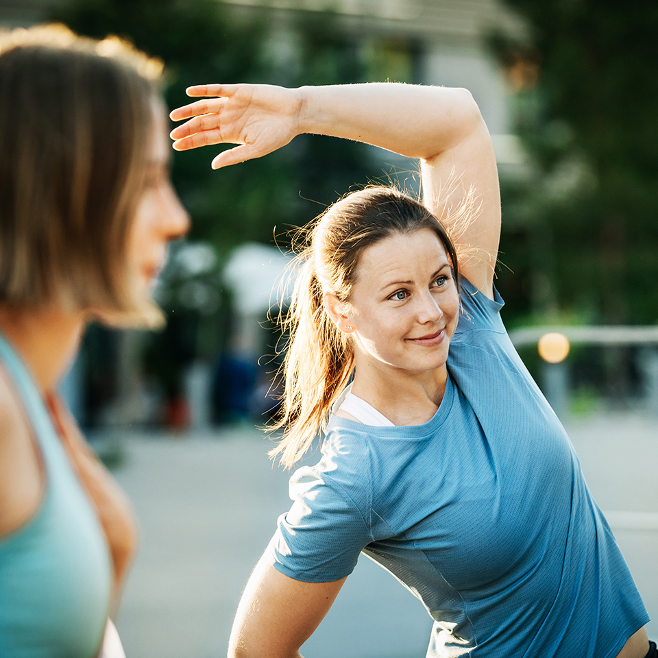 Young woman with hair in a ponytail raises arms above head while stretching