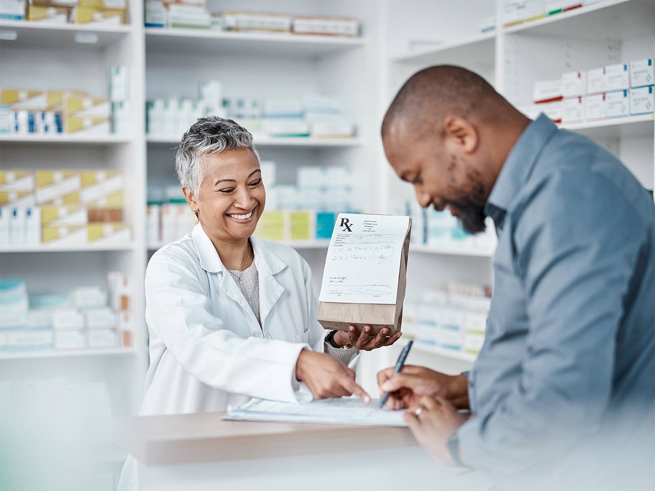 Smiling Corewell Health Specialty Pharmacy team member hands a paper bag containing a prescription to a smiling patient
