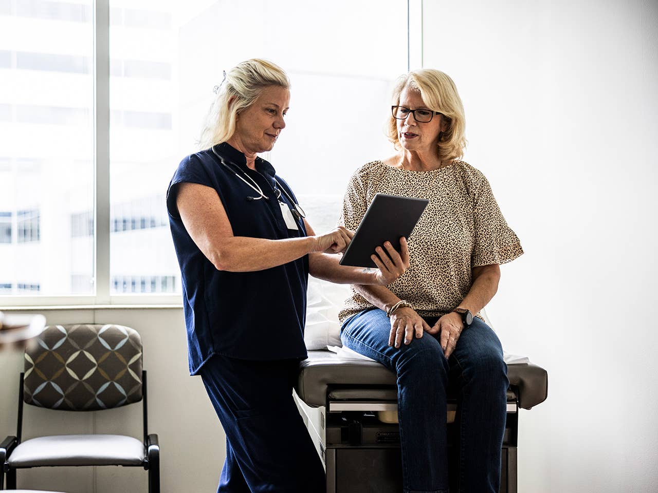 Older white woman sits on an exam table while speaking with a Corewell Health cancer care specialist