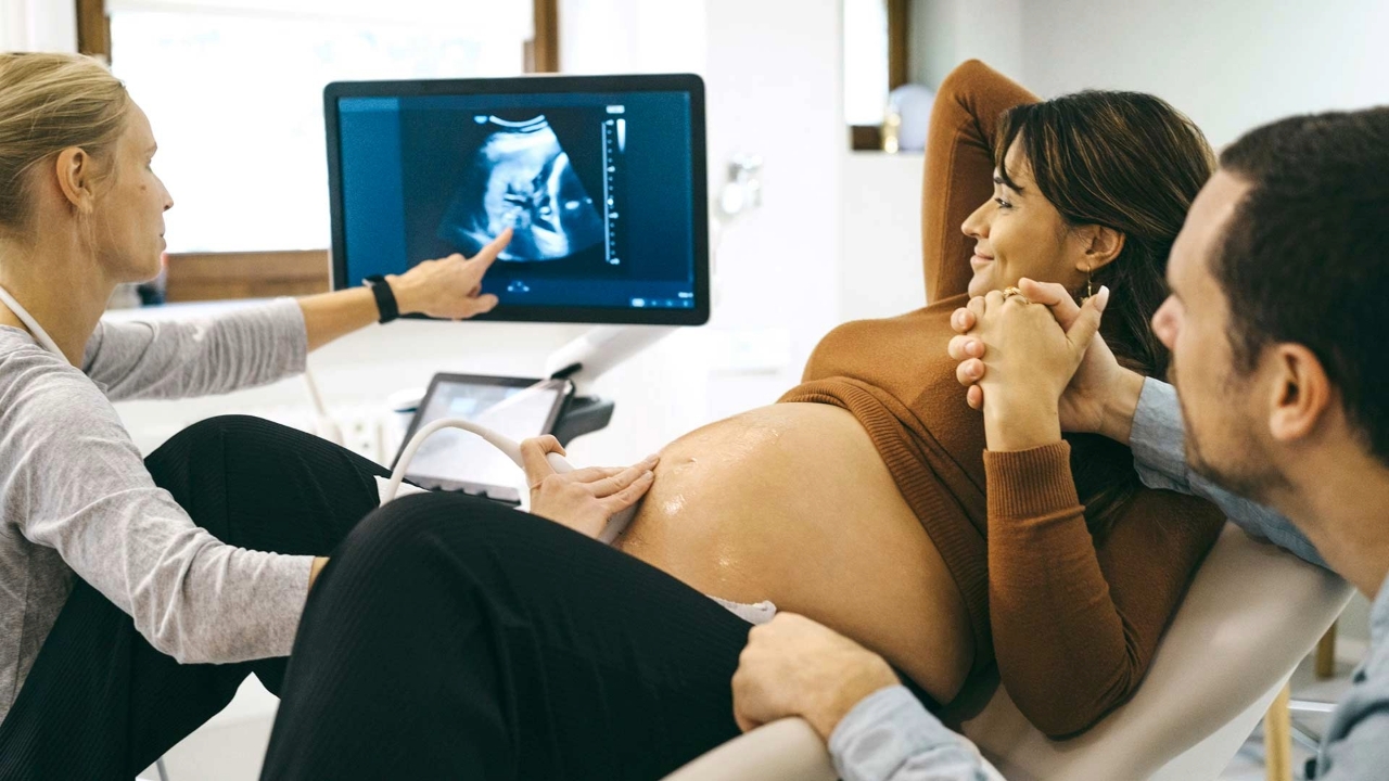Smiling young man and woman hold hands while looking at the screen of an ultrasound machine