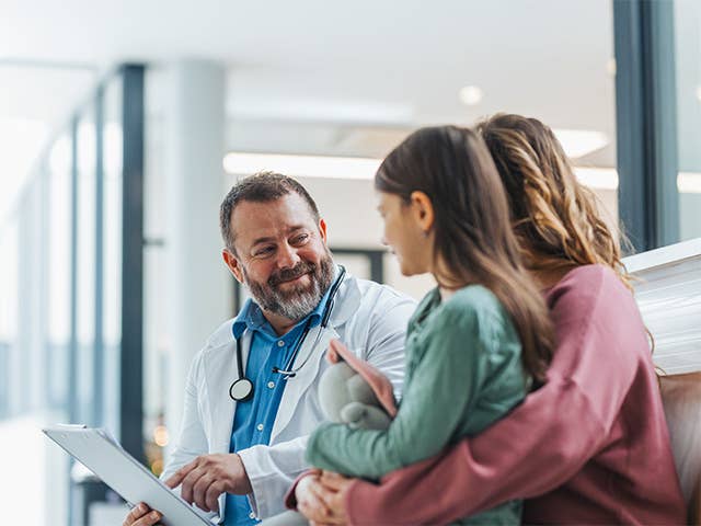 male medical provider speaking to a mother and her child while pointing at a medical chart in his hand