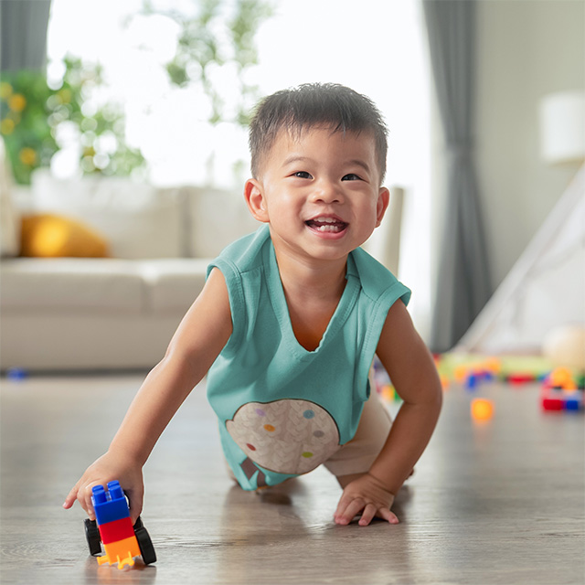 Young Asian boy sits on the floor on his knees while he plays with a plastic block