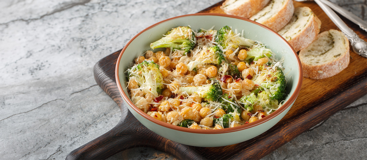 Bowl of cheesy chickpea and broccoli bake topped with grated cheese, served as a hearty plant-based meal.