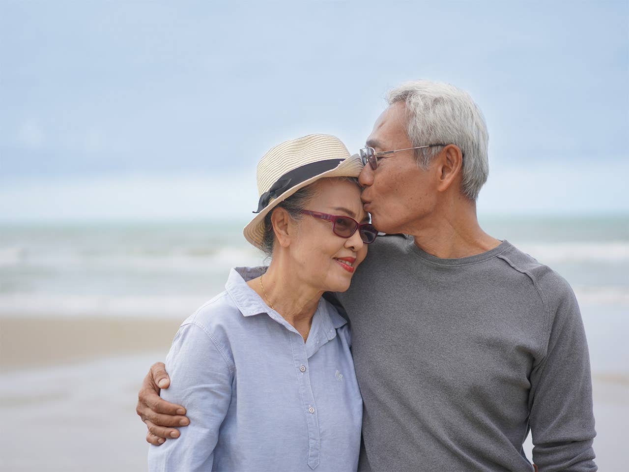 Older Asian man with grey hair and glasses hugs and kisses his wife