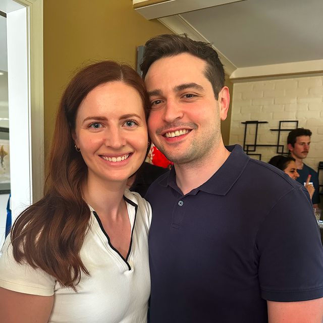 Two attendees pose together indoors at a social gathering.