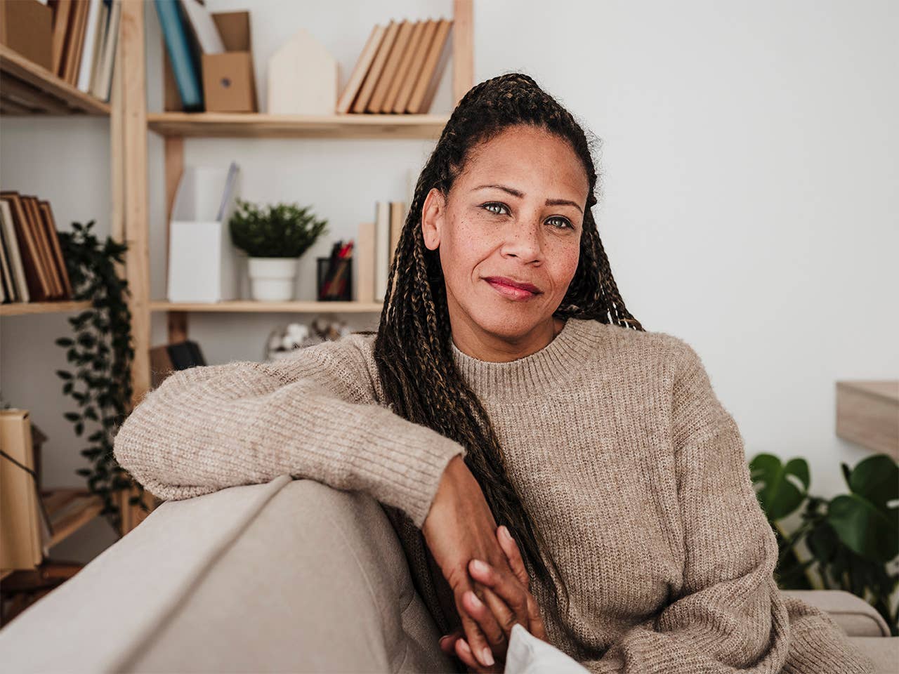 Black woman with long braided hair sits on a couch, resting her arm on the back of it