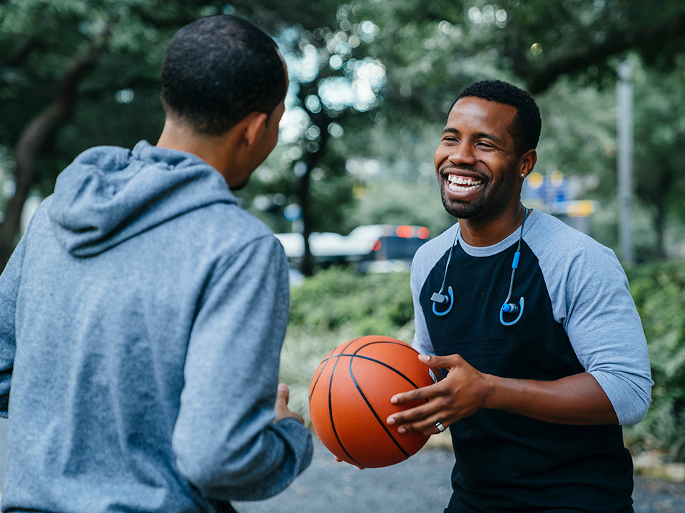 Two smiling Black men play basketball outdoors