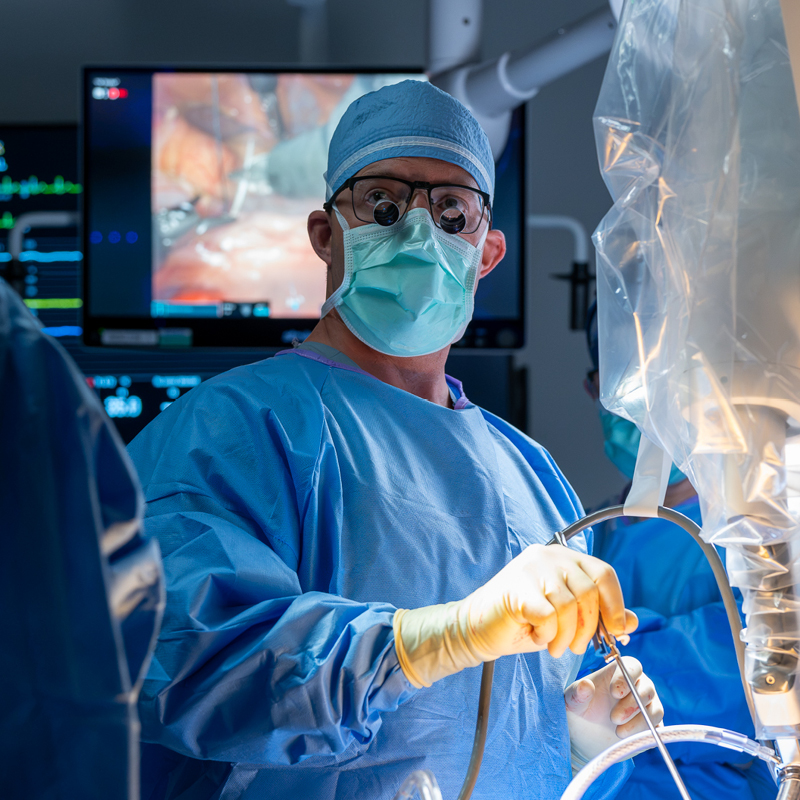 Surgeon wearing protective equipment and magnifying loupes performing a minimally invasive procedure in an operating room.