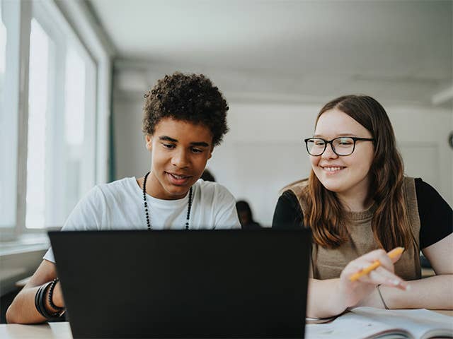 Two young individuals are focused on a laptop screen, engaged in a discussion or activity together.