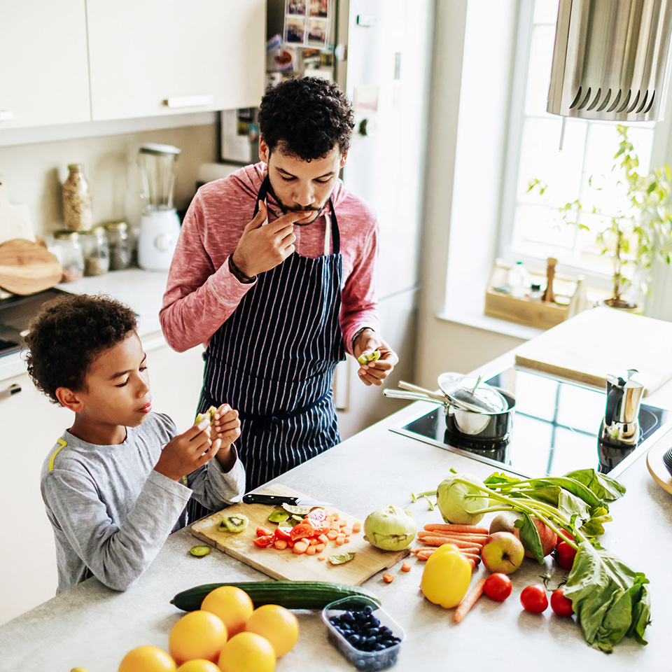 A dad and preteen son cutting up vegetables in the kitchen