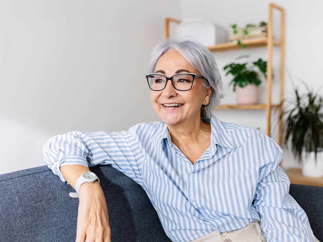 White woman with grey hair and glasses sitting on a sofa and resting her arm on the back of it